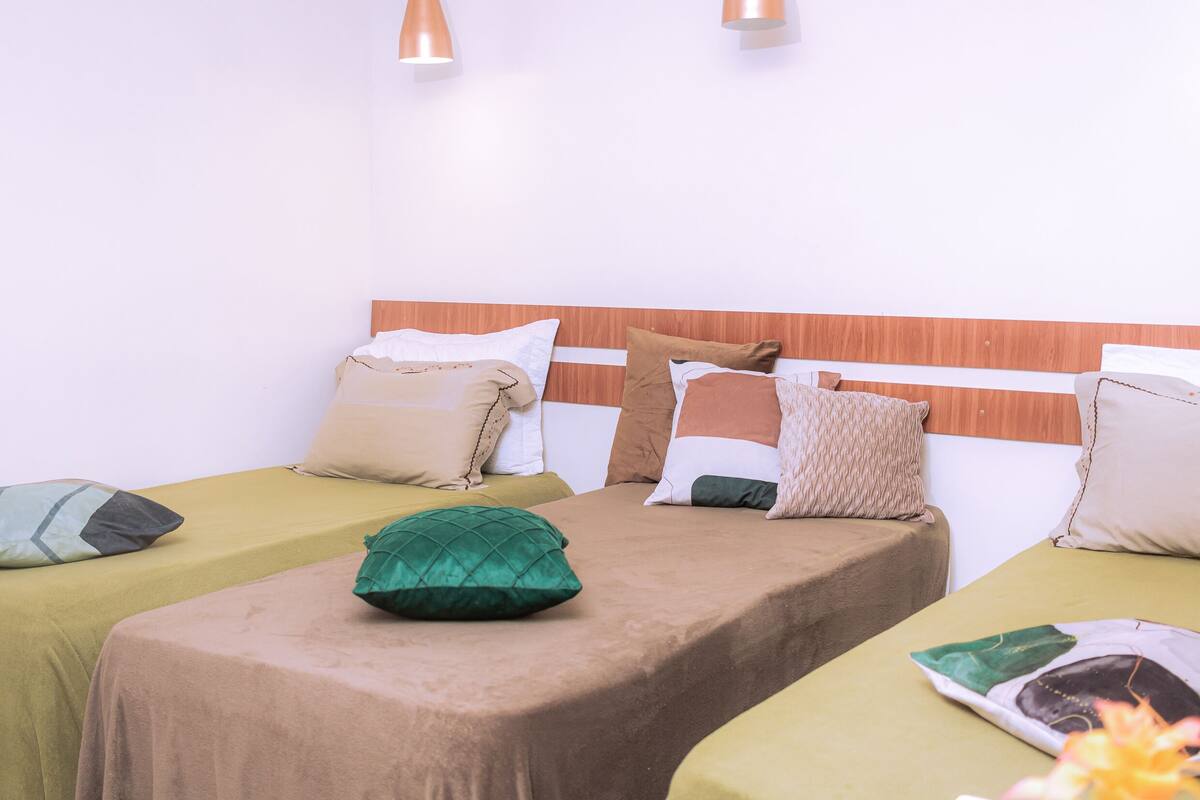 A hotel room with two beds, each with a different colored bedspread, multiple pillows, and a wooden headboard.