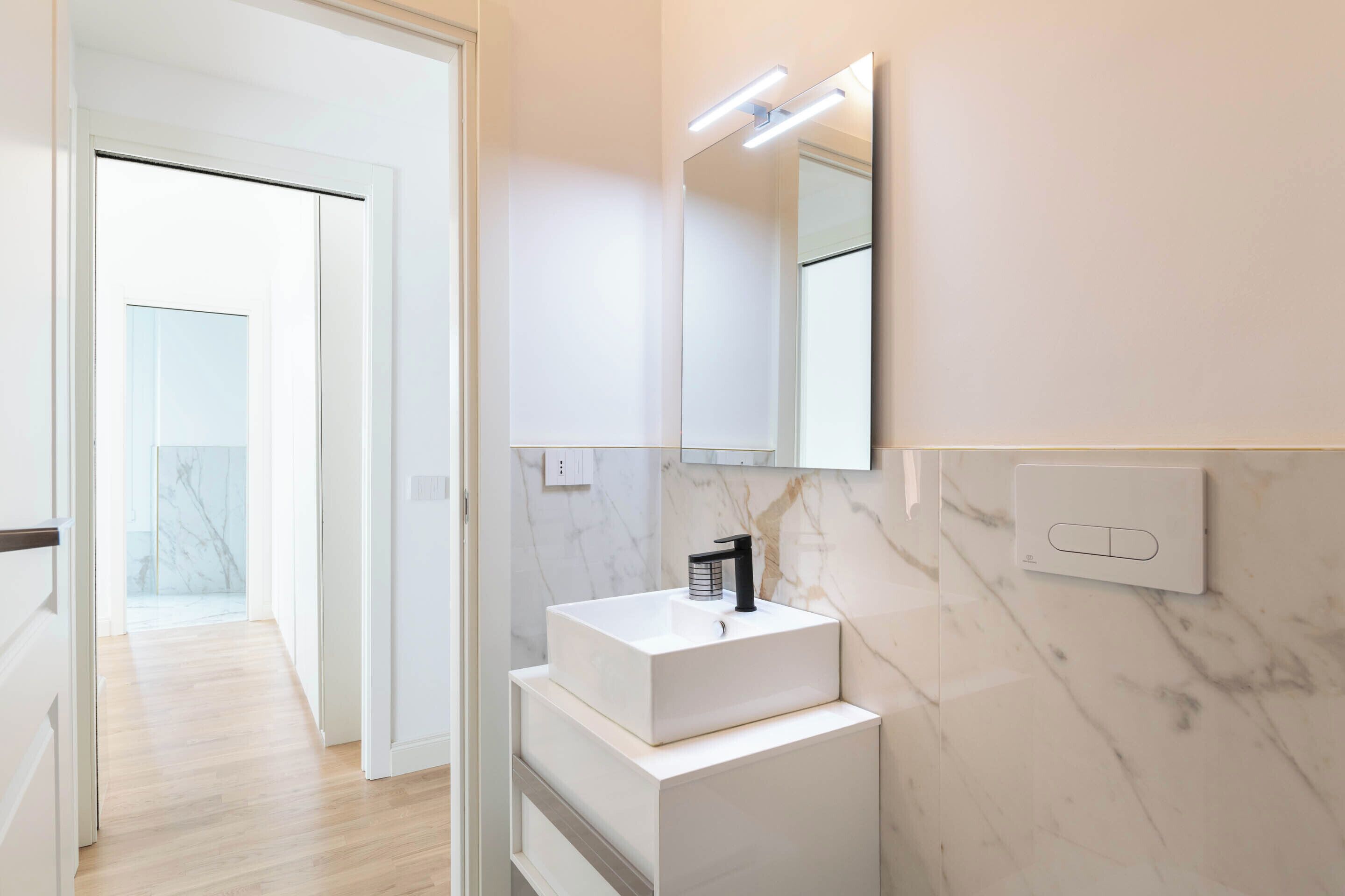 Un bany modern amb un lavabo blanc, un mirall gran i una cantonera de marbre.