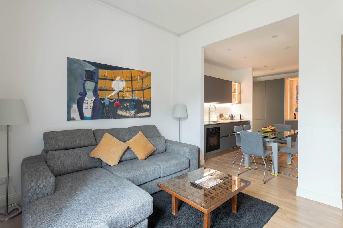 Un salon moderne avec un canapé d’angle gris, une table basse en bois et un tableau accroché au mur.