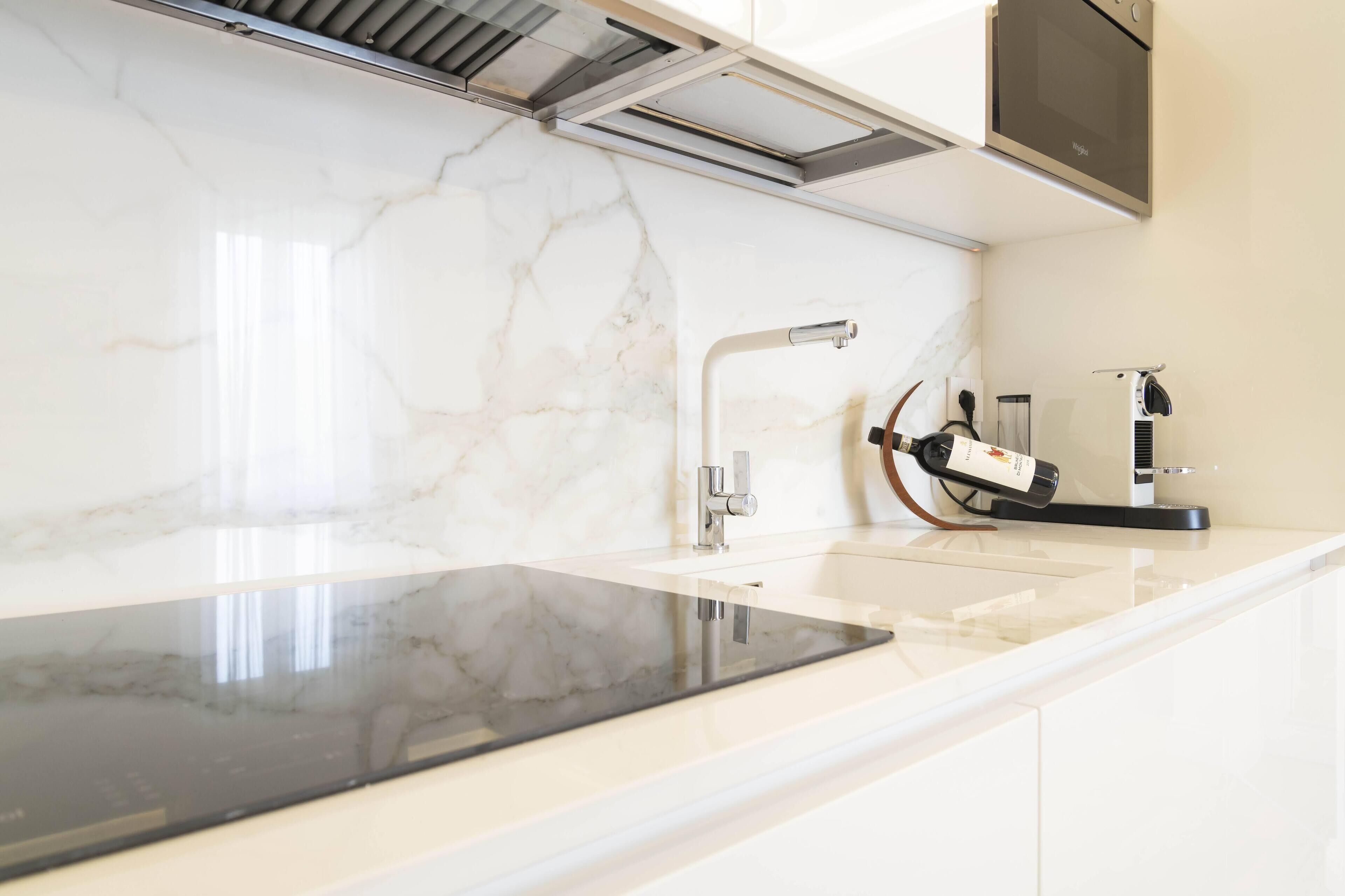 A modern kitchen with a marble backsplash, a black induction cooktop, and a built-in oven.