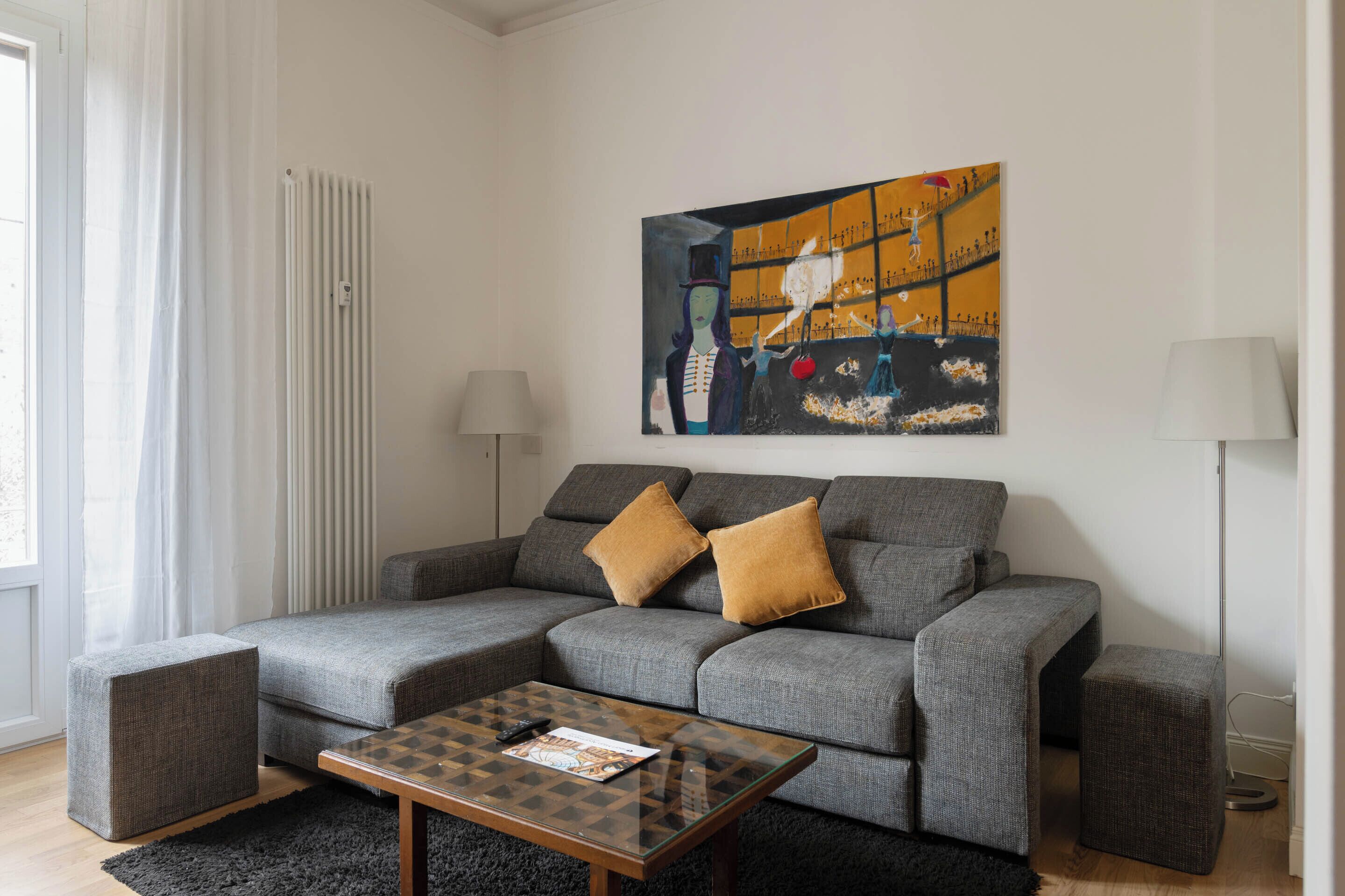 Una sala de estar moderna con un sofá seccional gris, dos otomanas, una mesa de centro de vidrio y un cuadro en la pared.