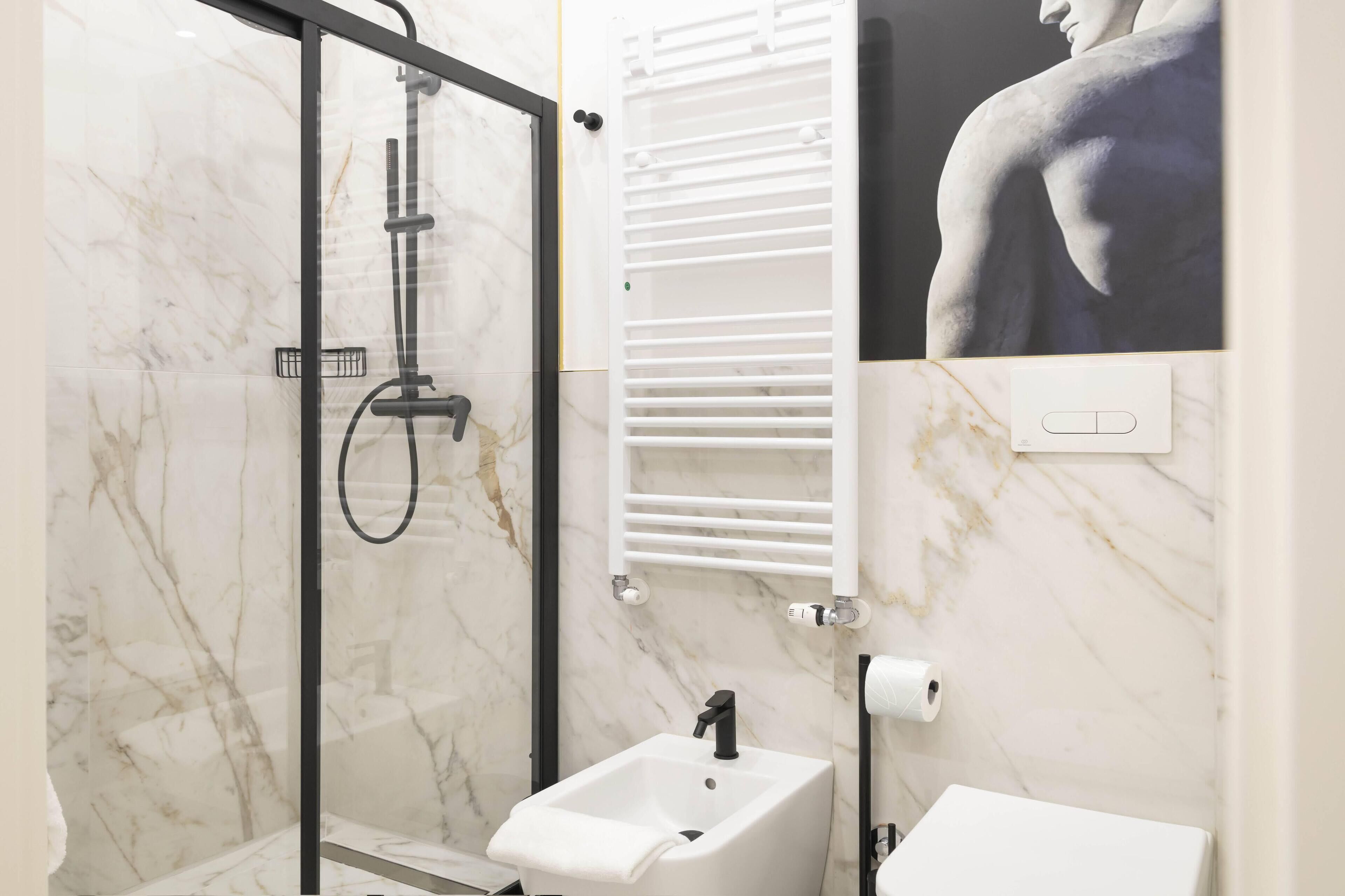A modern bathroom with a glass-enclosed shower, a white sink, and a marble-tiled wall.