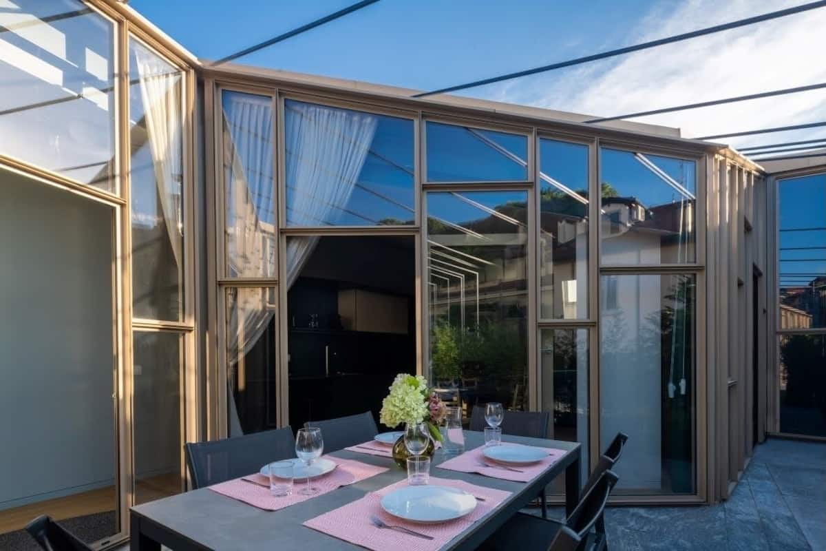 Un coin repas avec une table dressée pour quatre personnes, de grandes fenêtres en verre et une vue sur l’extérieur.