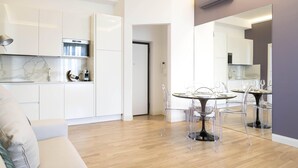 Une cuisine moderne avec des meubles blancs, un plan de travail en marbre et un coin repas comprenant des chaises transparentes et une table ronde.