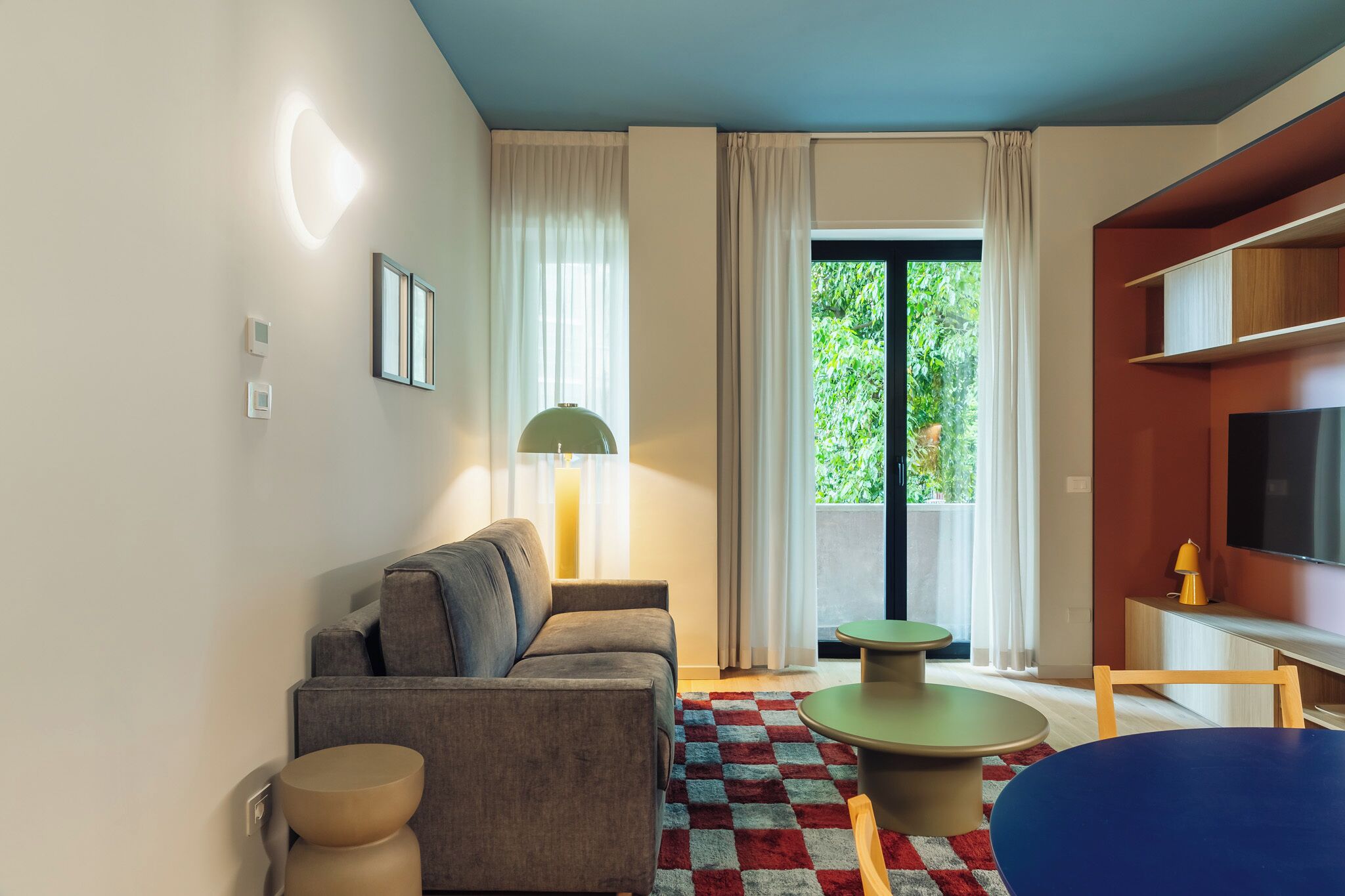 Una sala de estar moderna con un sofá, una mesa de centro, un televisor y un ventanal con cortinas.