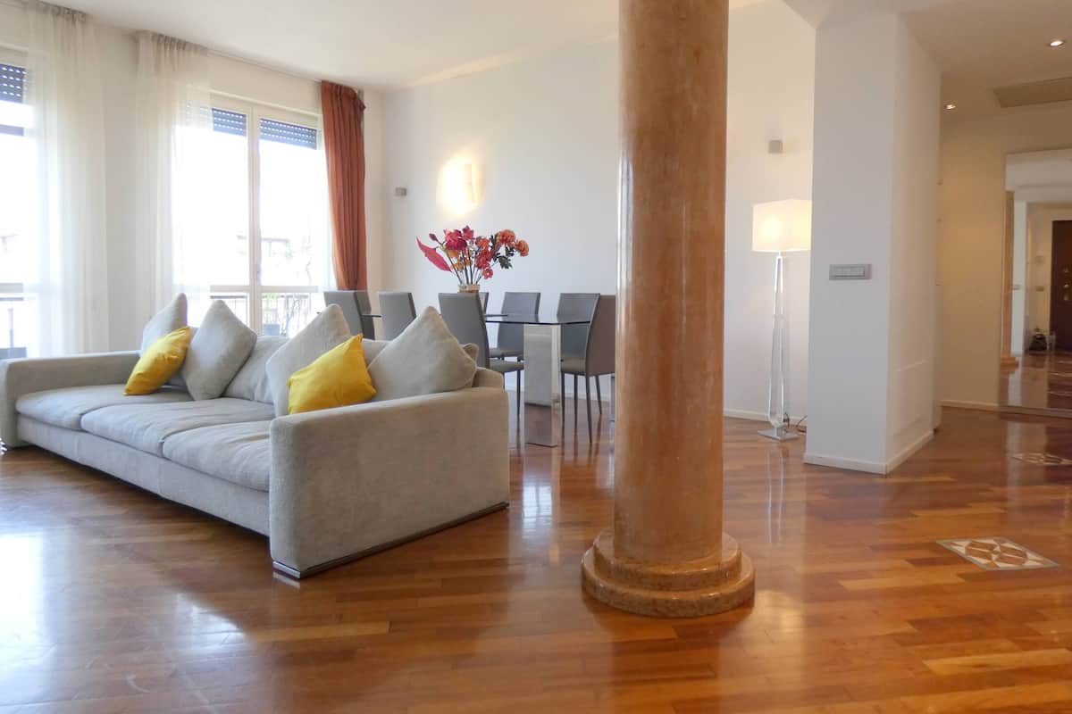 Un salon moderne avec un canapé gris, des coussins jaunes, une table à manger avec des chaises et une grande colonne.