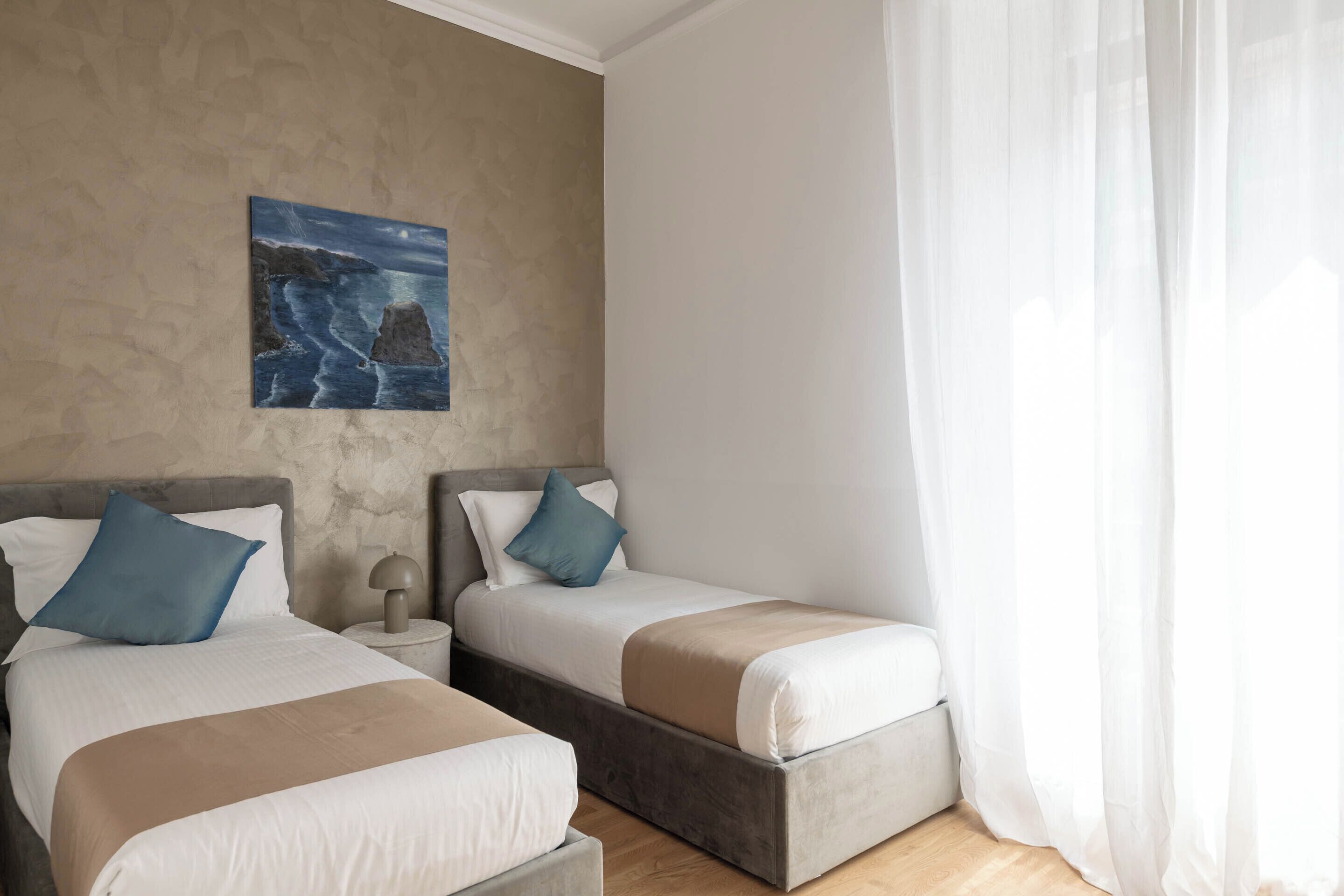Una habitación de hotel con dos camas, un cuadro en la pared y cortinas translúcidas.