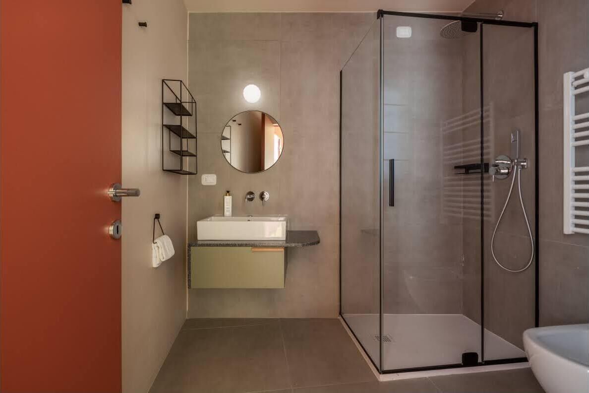 A modern bathroom with a glass shower enclosure, a white sink with a mirror above, and a towel rack.