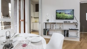 Un salon moderne comprenant un coin repas, un téléviseur à écran plat fixé au mur et une bibliothèque remplie de livres et d’objets décoratifs.