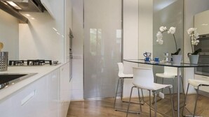 Une cuisine moderne avec des meubles blancs, une table à manger en verre et des chaises blanches.