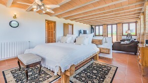Quarto amplo com uma cama grande, um banco de madeira, um ventilador de teto e vista para o exterior por grandes janelas.