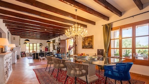 Uma sala de jantar espaçosa com mesa de vidro, cadeiras e um lustre.
