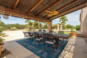 Relax in a serene outdoor space with a rustic table and chairs, surrounded by lush greenery and a soothing fountain.