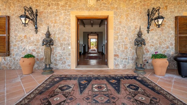 Uma entrada com paredes de pedra, piso ladrilhado, duas estátuas e um tapete estampado.