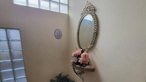 Ein Zimmer mit einem großen Spiegel, einem Blumentopf und einem Fenster mit Jalousien.