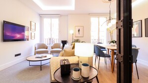 A modern living room with a flat-screen TV, comfortable seating, a dining area, and a large window. - Justicia Royal by Madflats Collection (Madrid)