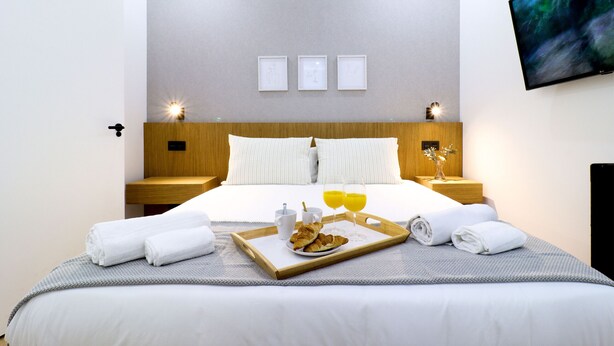 A hotel room with a large bed, a tray with croissants, juice, and a cup, and a TV mounted on the wall. - Justicia Royal by Madflats Collection (Madrid)