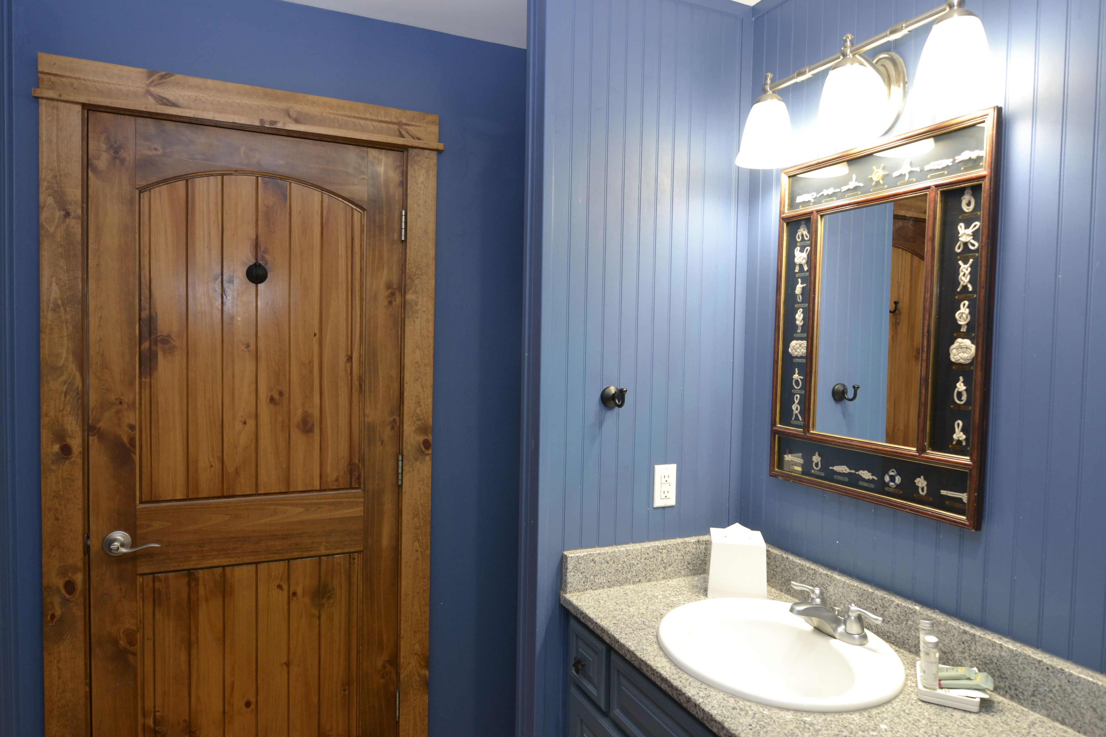 A bathroom with a wooden door, a sink with a granite countertop, and a mirror with a decorative frame.