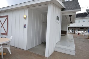Un bâtiment blanc doté d’un espace extérieur abrité avec des sièges, d’une porte et d’une petite fenêtre.
