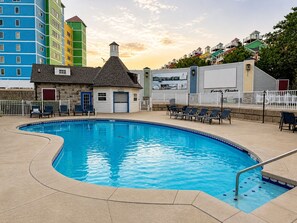 Une piscine avec des chaises longues, un petit bâtiment doté d’une cheminée, et, au fond, des immeubles résidentiels aux couleurs vives.