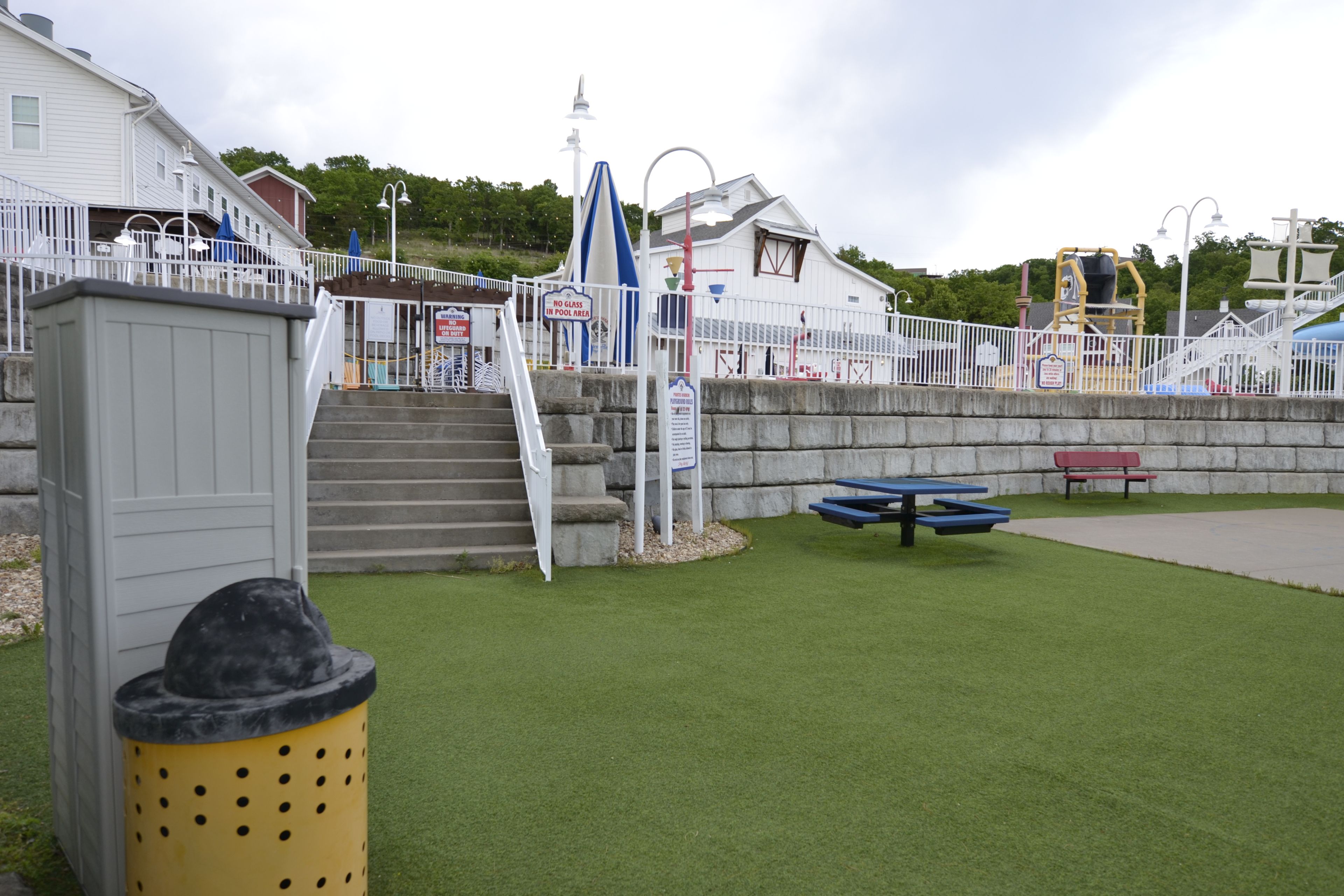 A waterfront park with a picnic table, a trash bin, and a playground.