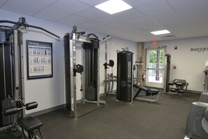 A gym with various exercise equipment, a poster on the wall, and an exit sign.