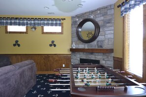 A room with a foosball table, a sofa, a fireplace, and a window with curtains.