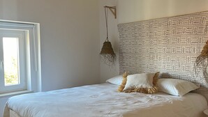 Un dormitorio con estructura de cama de madera, ropa de cama blanca, pared con estampado y una lámpara colgante.