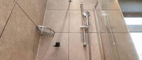 A bathroom with a shower, a handheld showerhead, a handheld shower nozzle, and a shower head.