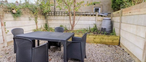 An outdoor patio with a table and chairs, surrounded by gravel and plants.