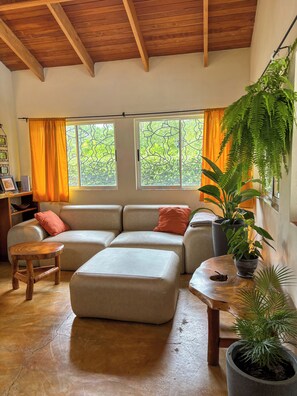A living room with a sectional sofa, a wooden coffee table, a small stool, and a potted plant.