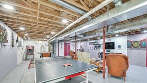 A ping pong table in a room with exposed wooden beams, a dartboard, and a television.