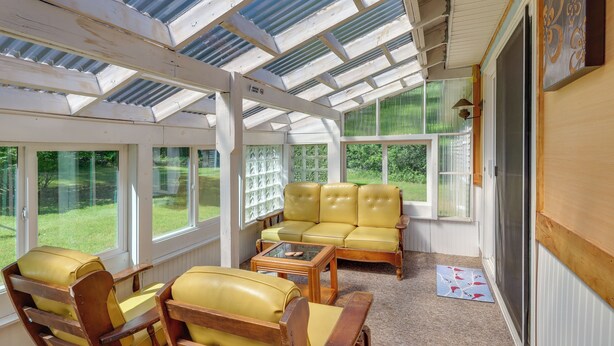 A sunroom with a glass ceiling, yellow leather sofa, wooden chairs, and a small table.