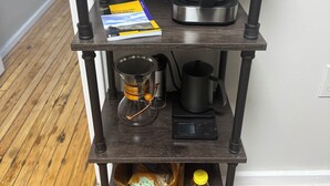Een houten plank met een koffiezetapparaat, een boek, een glazen kan, een weegschaal, een houten kom en een pot honing.