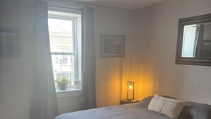 Een slaapkamer met een groot bed, een bedlampje, een raam met gordijnen en een ingelijste foto aan de muur.