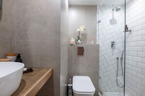 Un baño moderno con tocador de madera, inodoro blanco y zona de ducha con mampara de vidrio.