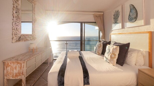 A bedroom with a large bed, a dresser, and a view of the sea.