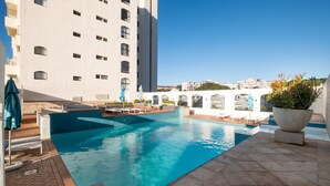 A rooftop pool area with a clear blue pool, lounge chairs, and a potted plant.