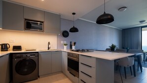 A modern kitchen with a built-in washer, oven, and microwave, a large island with seating, and a dining area with a view. - Umhlanga Ridge | Pool | Sauna | Aircon |Gym (Cape Town)