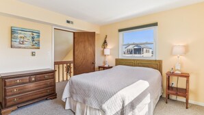Un dormitorio con una cama grande, un aparador de madera, un cuadro en la pared, una ventana con vistas y dos lámparas de noche.