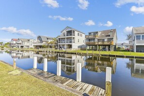 A waterfront residential area with houses along a canal, wooden docks, and a clear sky.