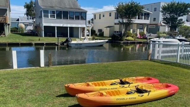 Dos kayaks en un área de césped cerca de un cuerpo de agua, con barcos amarrados al fondo.