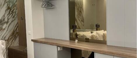 A modern bedroom with built-in storage, a vanity with a mirror, and a marble-patterned wall.