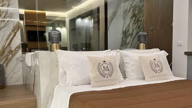 Un dormitorio moderno con una cama grande, paredes de mármol y un separador de vidrio.