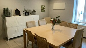 Een eetgedeelte met een houten tafel en stoelen, een wit kastje en een raam met natuurlijk licht.