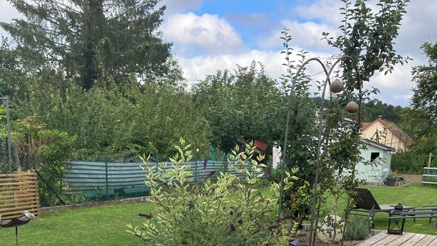 Een buitenzwembad omgeven door een tuin met een houten terras en een kleine schuur op de achtergrond.
