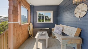 Un porche cubierto con un banco y una mesa de madera, una ventana con vistas, y un aplique de pared.