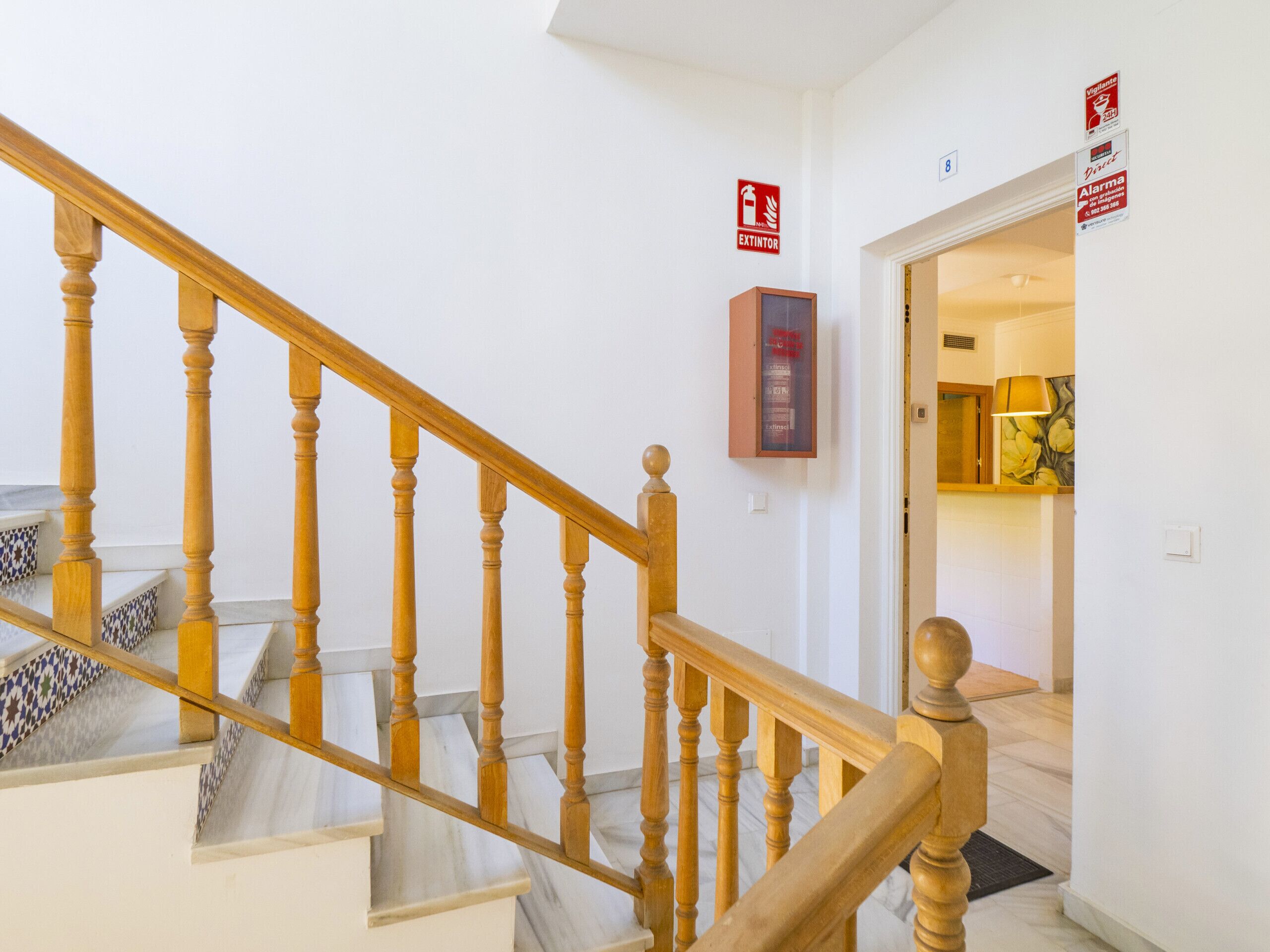 A wooden staircase with a fire extinguisher and an emergency exit sign on the wall.