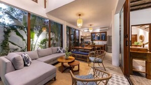 A modern living room with a sofa, coffee table, and wicker chairs. There is a kitchen area in the background with a dining table and chairs. - Entire villa for 8 people (El Paredon)