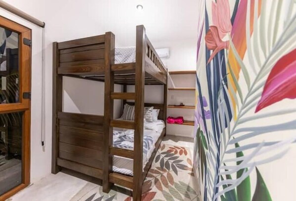 A bunk bed room with a wooden ladder, a small shelf, and a colorful leaf-patterned wall.
